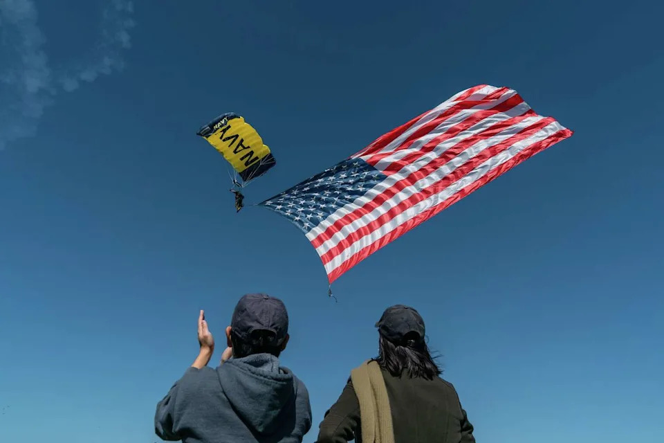 Spectators cheer on the arrival of the American flag carried by a member of the U.S. Navy 