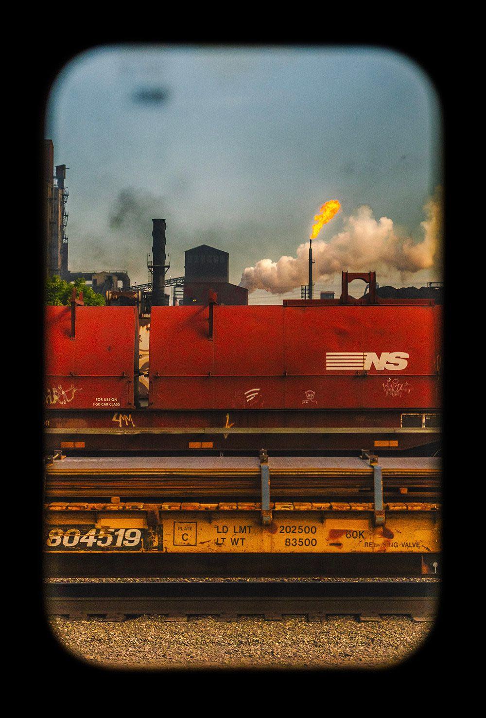 Smoke rises from a factory behind a red railway carriage